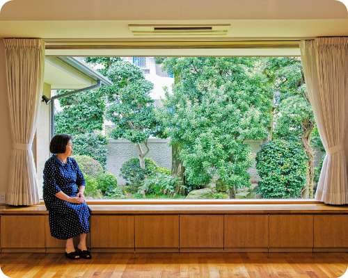 写真：大きな窓辺に腰をかけて外を眺める女性